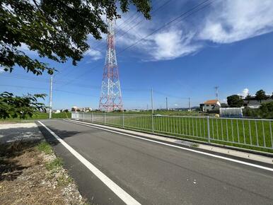 敷地と道路の境界付近より、南東方向へ撮影した写真です。道路の向かい側には白色の柵が設置されています。