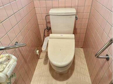 洗面所と同じピンクのタイルのトイレ。温水洗浄暖房便座で手すりもあります。