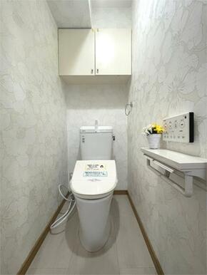 清潔感あふれるトイレは、爽やかな花柄の壁紙が印象的。吊戸棚や飾り棚も設置され、収納力と使いやすさを両