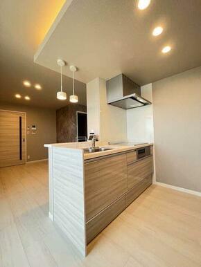 【システムキッチン】対面キッチンでペンダントライトが備え付けてあり、明るいトーンのキッチンとなって…