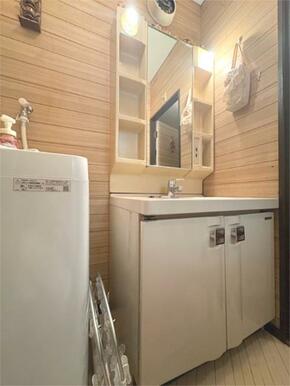 木目調の壁が温かみを感じさせる洗面所。洗面台には鏡裏収納があり、小物の整理に役立ちます。洗濯機置き場