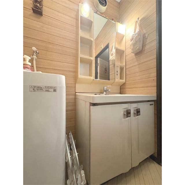 木目調の壁が温かみを感じさせる洗面所。洗面台には鏡裏収納があり、小物の整理に役立ちます。洗濯機置き場