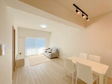 LD　別角度の写真です。窓からバルコニーへ出ることができます。キッチン付近にニトリ家具の机と椅子があり、ダウンライトが照らしています。