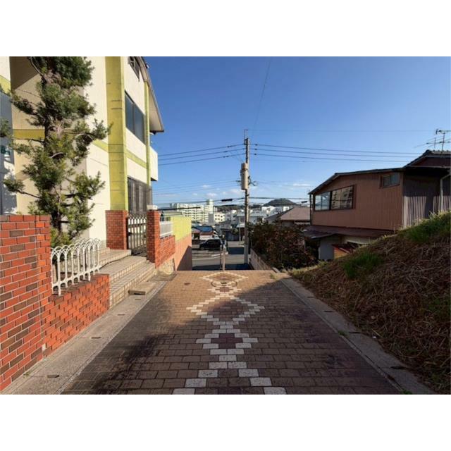 青空が広がる日差し明るい現地。前面道路は舗装されており、住宅街の中を穏やかに下っていく坂道です。