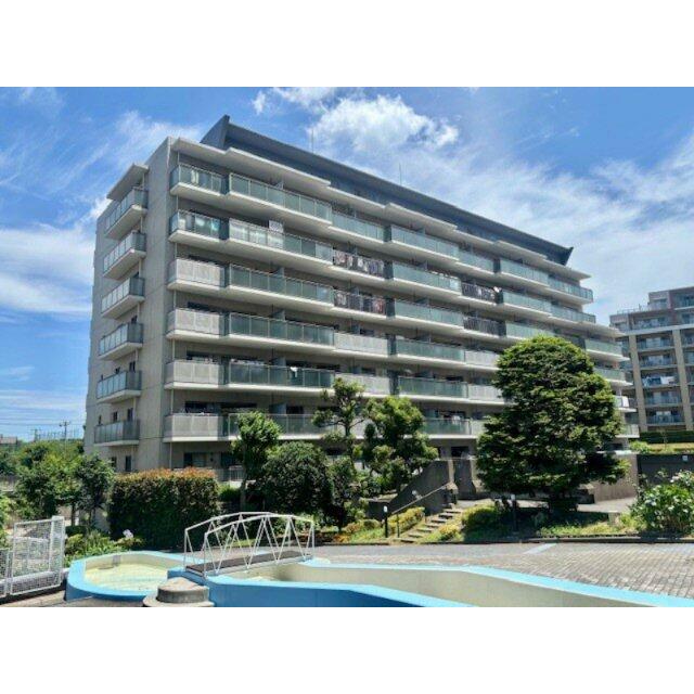 ベージュ系のタイル貼りの外観で、バルコニー立ち上がりのガラスパネルが特徴です。2025年6月撮影