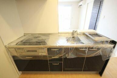 対面型システムキッチン。ガスコンロ３口・グリル付き。建具に合わせたダーク色。