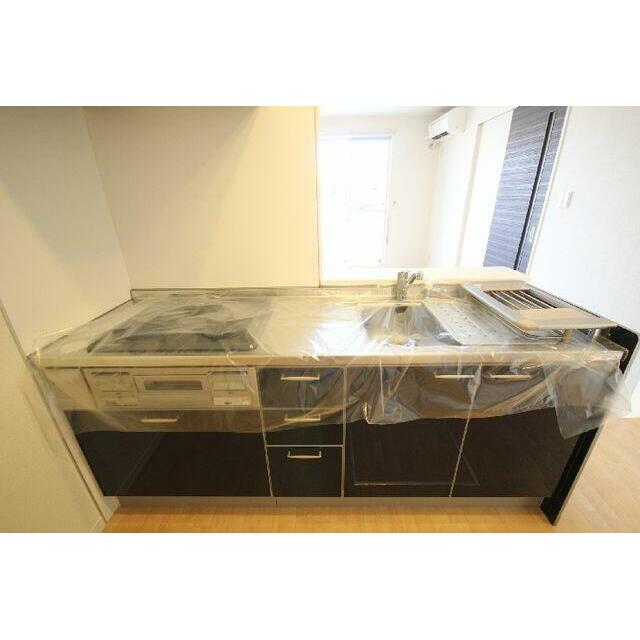 対面型システムキッチン。ガスコンロ３口・グリル付き。建具に合わせたダーク色。