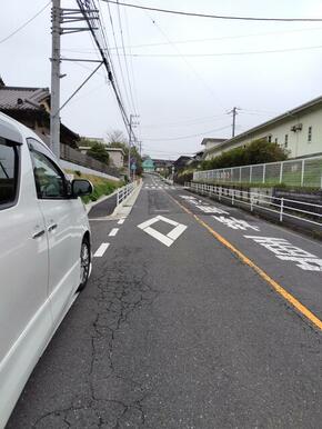 家の前のバス通り、この先、緑の家の手前、右手の白い駐車場が目印